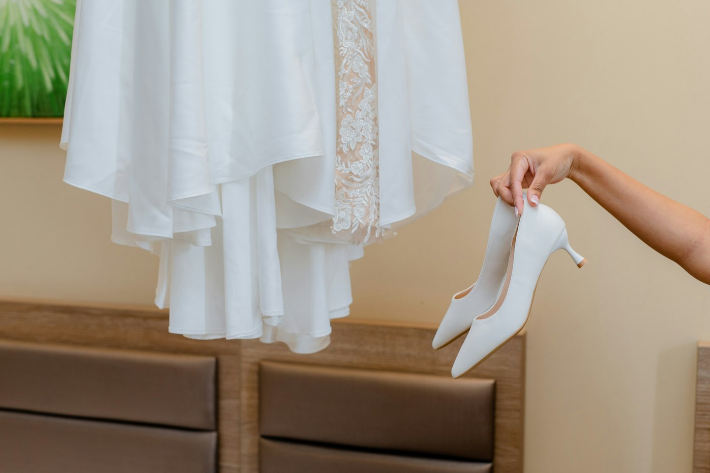 Bridal lace dress hangs near high heels for a wedding.